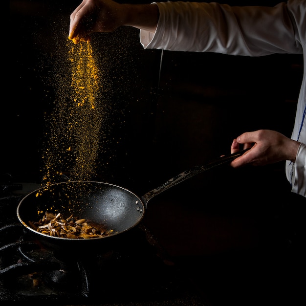 Free photo side view mushroom frying with stove and spice and human hand in pan