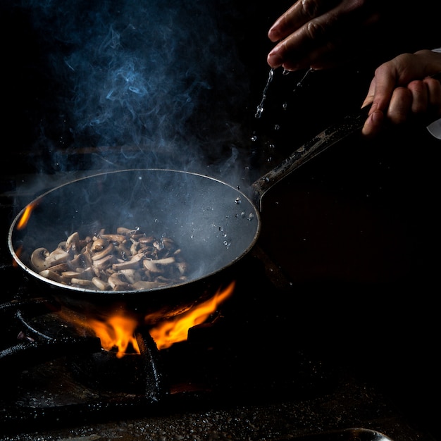 Side view mushroom frying with water drop and fire and human hand in pan