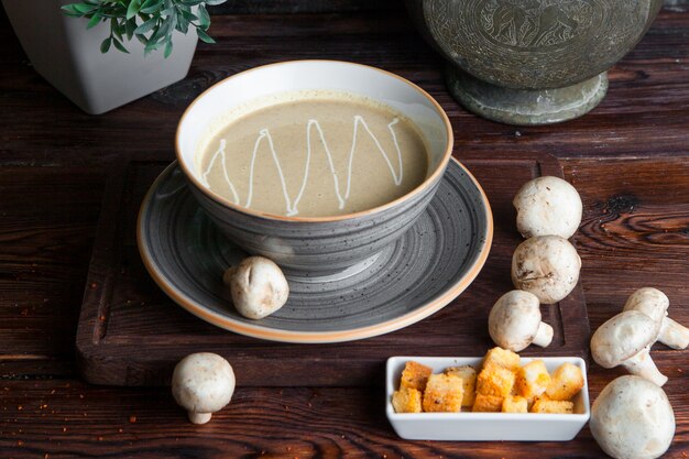 Side view mushroom soup with champignon and crackers in plate on wooden table