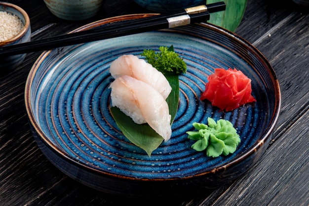 Side view of nigiri sushi on bamboo leaf served with ginger and wasabi on a plate