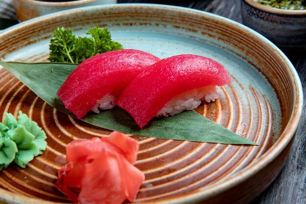 Side view of nigiri sushi with tuna on bamboo leaf served with pickled ginger slices and wasabi on a plate