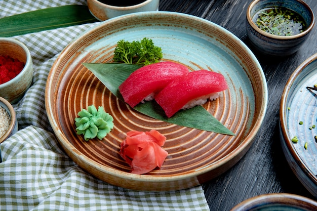 Side view of nigiri sushi with tuna on bamboo leaf served with pickled ginger slices and wasabi on a plate