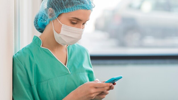 Side view nurse with mask checking mobile