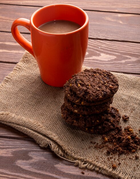 Side view of oatmeal cookies with chocolate chips and cocoa and a mug with cocoa drink on a wooden