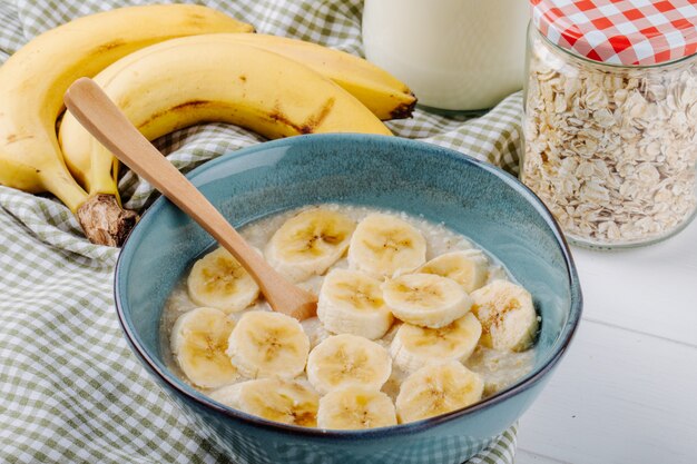 Side view of oatmeal porridge with banana in a ceramic bowl on rustic table