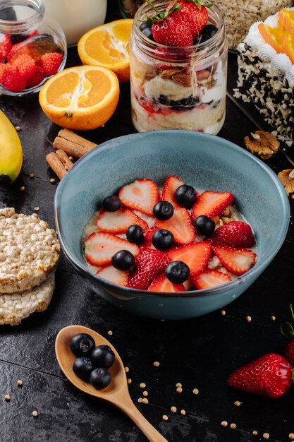 Side view of oatmeal porridge with sliced strawberries and blueberries in a ceramic bowl on the table