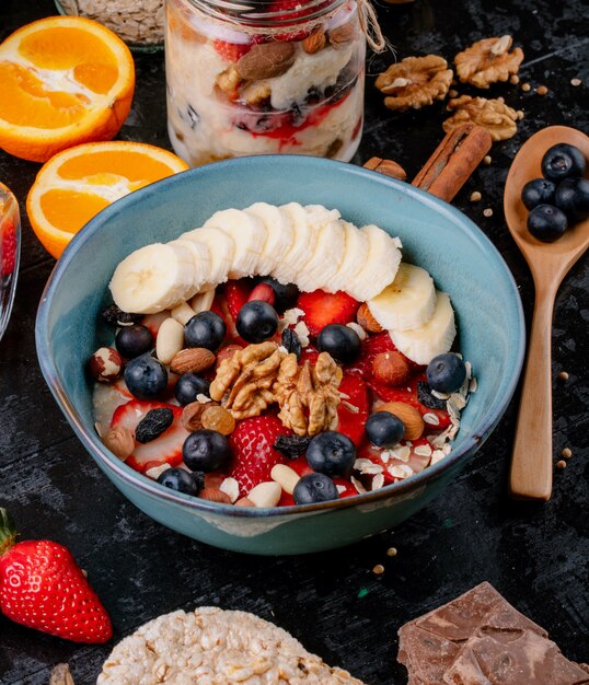 Side view of oatmeal porridge with strawberries blueberries bananas dried fruits and nuts in a ceramic bowl on the table