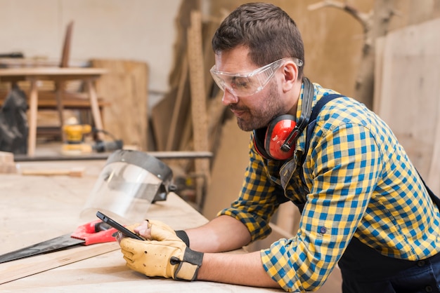 Бесплатное фото Вид сбоку мужского плотника с помощью мобильного телефона в мастерской