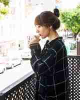 무료 사진 커피를 마시는 발코니에 서있는 여자의 모습