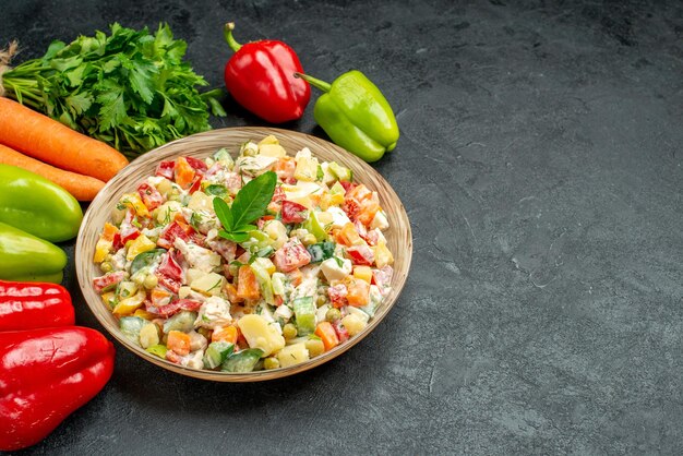 짙은 회색 테이블에 당근 채소와 피망을 곁들인 야채 샐러드 그릇의 측면 보기
