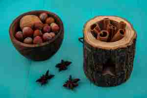 Бесплатное фото Вид сбоку корицы в миске из дерева и миске с орехами на синем фоне