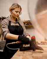 Бесплатное фото Женщина-плотник с пневматическим степлером в студии, вид сбоку