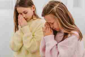 Бесплатное фото Маленькие девочки молятся дома, вид сбоку