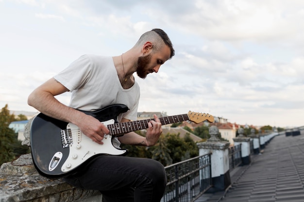 Бесплатное фото Вид сбоку мужчины-художника на крыше, играющего на электрогитаре