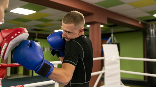 Бесплатное фото Вид сбоку на боксера-мужчину с тренером, тренирующегося рядом с рингом