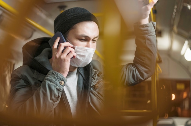 의료 마스크를 착용하는 동안 버스에서 전화로 얘기하는 사람의 측면보기