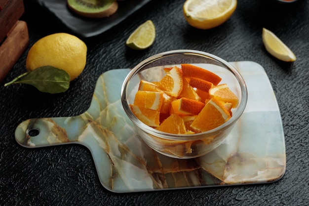무료 사진 검은 배경에 레몬이 있는 커팅 보드에 있는 그릇에 있는 오렌지 조각의 측면 보기