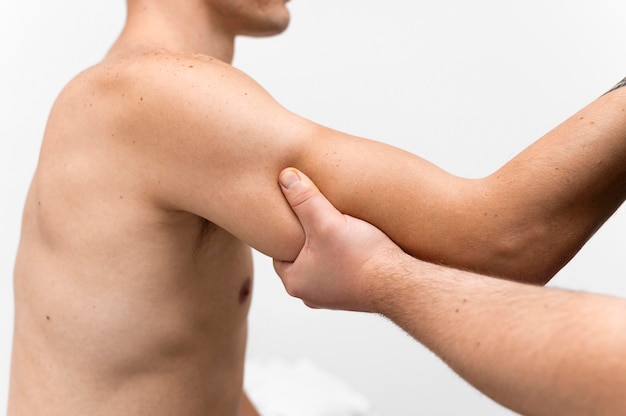 무료 사진 남자의 팔을 마사지하는 물리 치료사의 측면보기