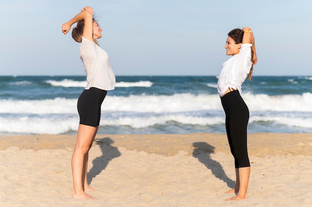 무료 사진 해변에서 운동하는 두 여자 친구의 측면보기
