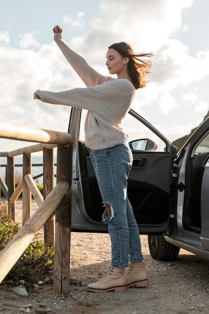 Бесплатное фото Вид сбоку на женщину, наслаждающуюся пляжным бризом рядом с автомобилем