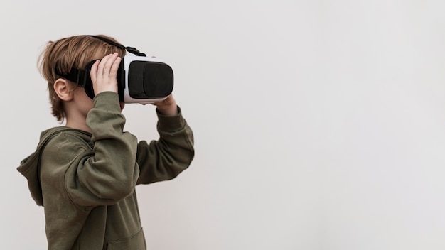 Бесплатное фото Вид сбоку мальчика, использующего гарнитуру виртуальной реальности с копией пространства