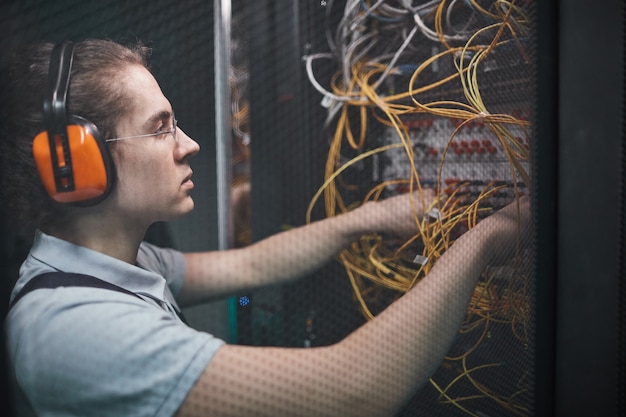 Вид сбоку молодого сетевого инженера, соединяющего кабели в серверной комнате во время технического обслуживания в центре обработки данных, копировальное пространство