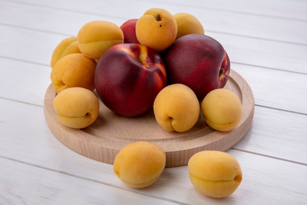 Side view ofpeaches with apricots on a stand on a white surface