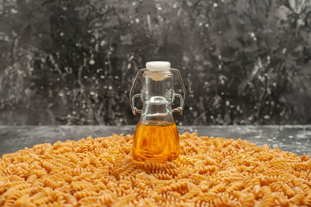 Side view of oil bottle standing on raw Italian pasta lined up in a circle on gray background