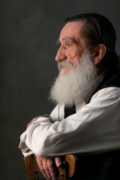 Side view old man with long beard on chair