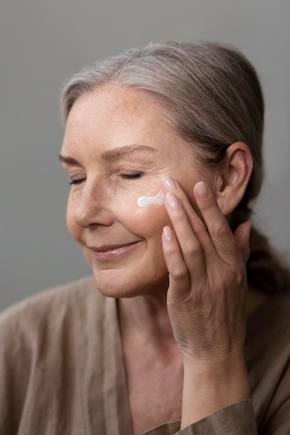 Foto gratuita donna anziana di vista laterale che applica crema per il viso