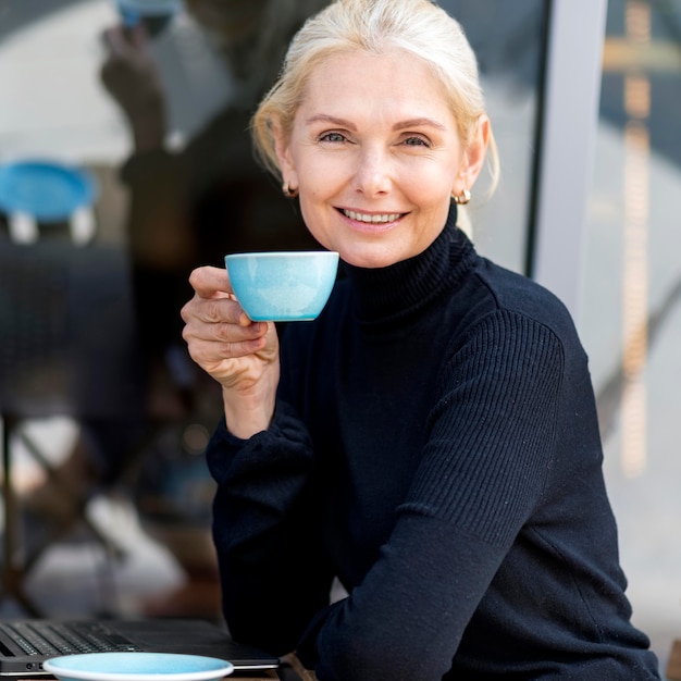 Side view of older business woman enjoying coffee outdoors while working