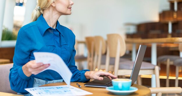 Вид сбоку пожилой деловой женщины, работающей на ноутбуке за чашкой кофе