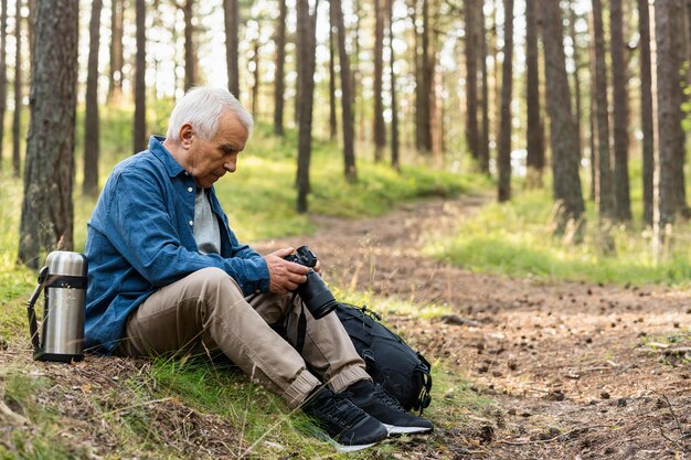 Side view of older man holding camera while resting in nature