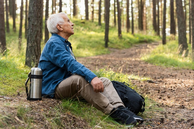 Free photo side view of older man resting and enjoying nature while backpacking