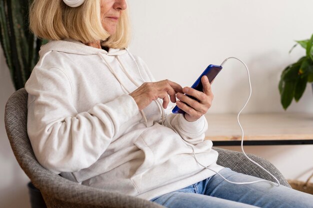 Вид сбоку пожилой женщины дома, слушающей музыку в наушниках