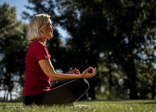 Side view of older woman in lotus position outdoors during yoga