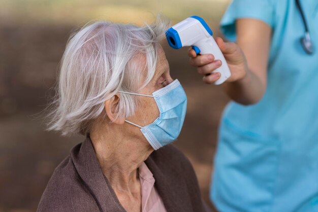 Вид сбоку пожилой женщины с медицинской маской, проверяющей ее температуру