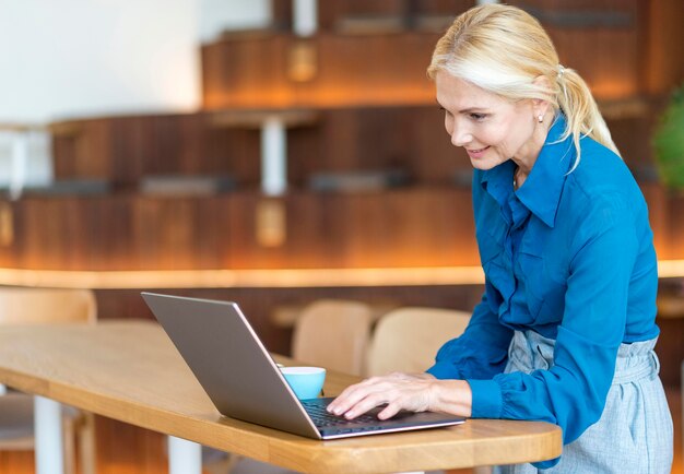 Side view of older woman working on laptop while having coffee