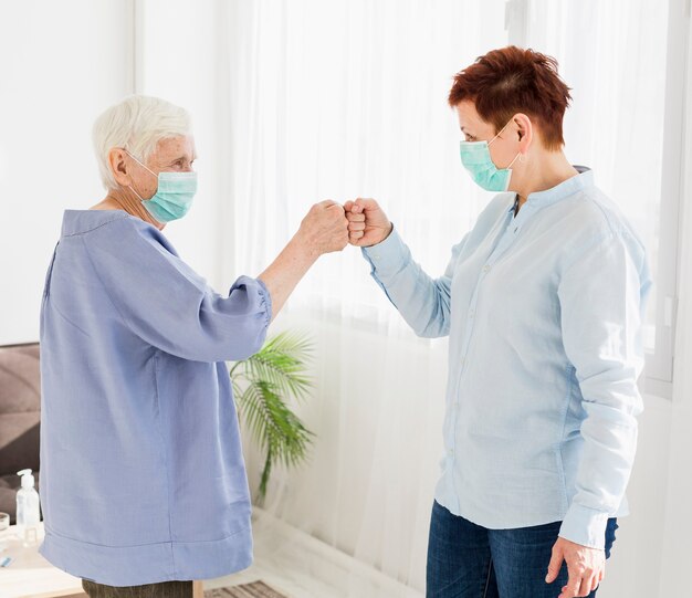 Side view of older women bumping fists while wearing medical masks