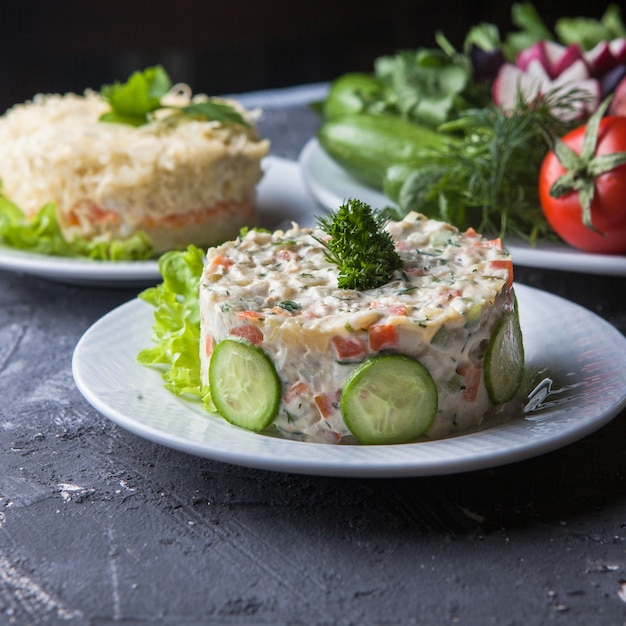 Side view olivier salad with mimosa salad and tomato and cucumber in round white plate