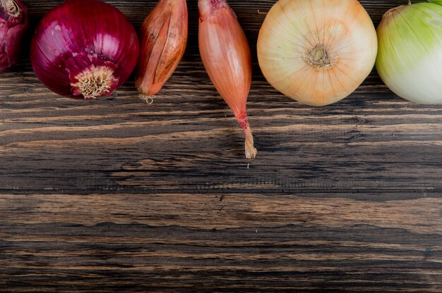 Side view of onions as red white shallot and sweet on wooden background with copy space