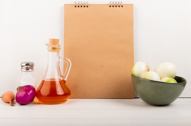 Side view of onions in bowl melted butter salt with note pad on wooden surface and white background with copy space