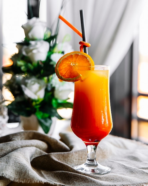Бесплатное фото Вид сбоку апельсиновый коктейль с ломтиком апельсина и соломкой в бокале