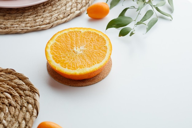 Side view of orange half on trivet with kumquat trivets and leaves on white background