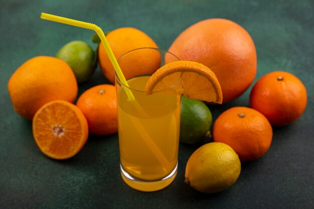 Апельсиновый сок сбоку в стакане с лаймом, лимоном, апельсинами и грейпфрутом на зеленом фоне