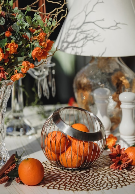 Side view of oranges in metal basket vase on the table