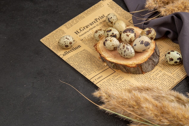 Free photo side view of organic eggs on a wooden board on an old newspaper spike black towel on dark surface