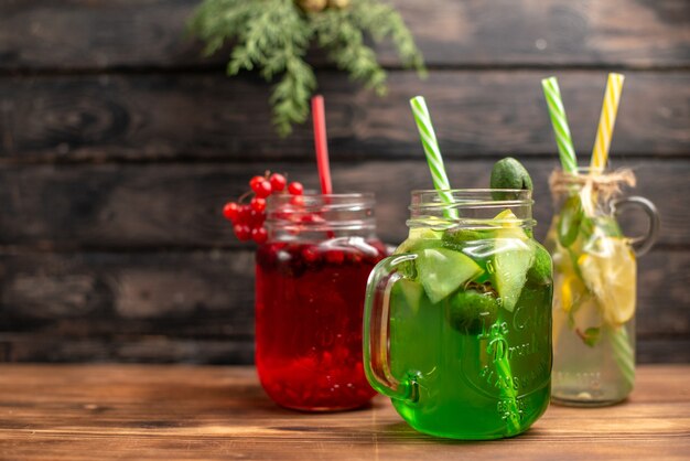 Side view of organic fresh juices in bottles served with tubes and fruits on the left side on a brown wooden background