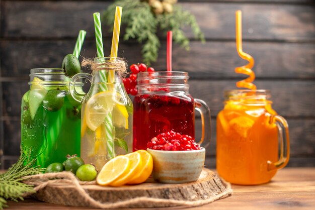 Side view of organic fresh juices in bottles served with tubes and fruits on a wooden cutting board