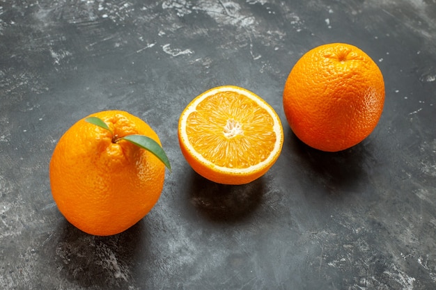 Side view of organic natural whole and cut fresh oranges with leaves on gray background